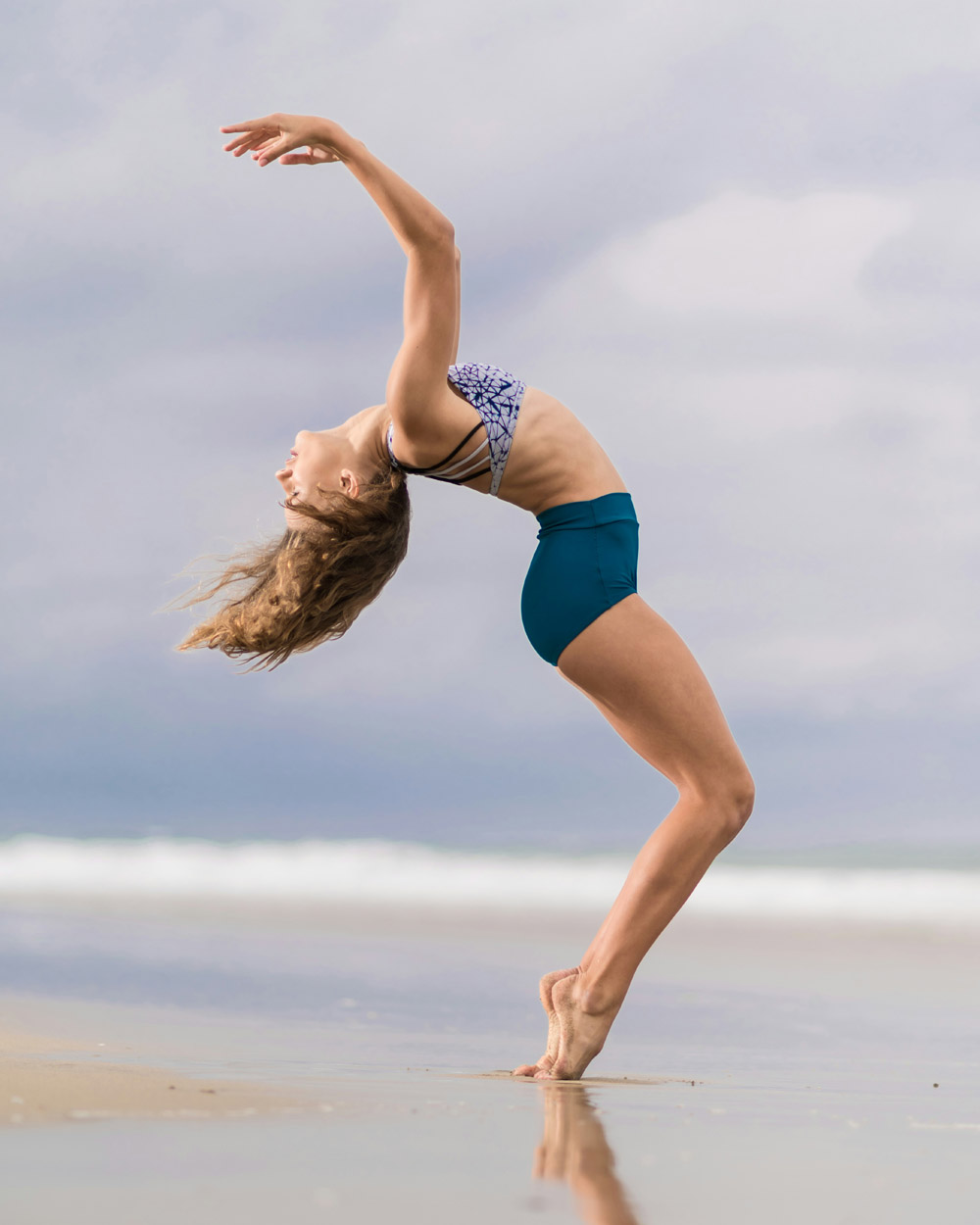 A woman viewed from the side, dancing on a sandy beach.